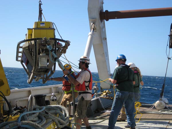 Crew maneuvering the sonar towfish over the vessel's starboard quarter.